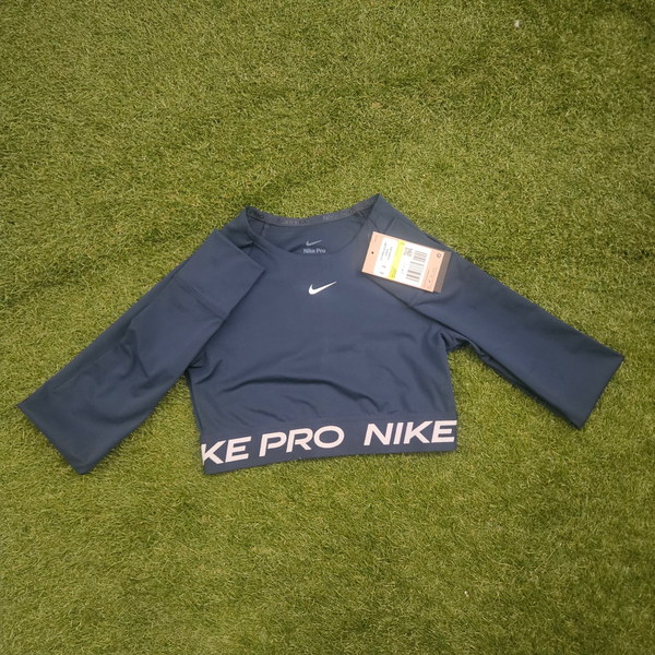 A navy blue Nike long-sleeve athletic shirt laid flat on green grass, with 'NIKE PRO' printed in white down one sleeve and a small white swoosh logo on the chest. A hangtag is attached near the neckline.